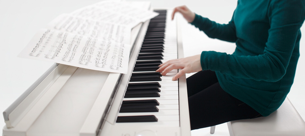 Photo of someone playing a digital piano with sheet music spread across the top of the piano