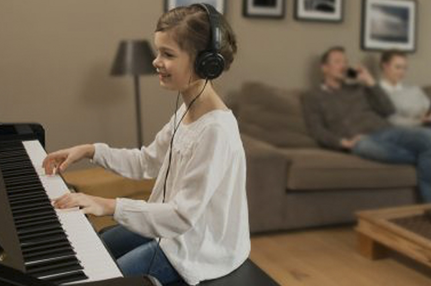 Photo of a child playing a Silent piano using headphones whilst her parents talk on the phone and watch TV in a living room