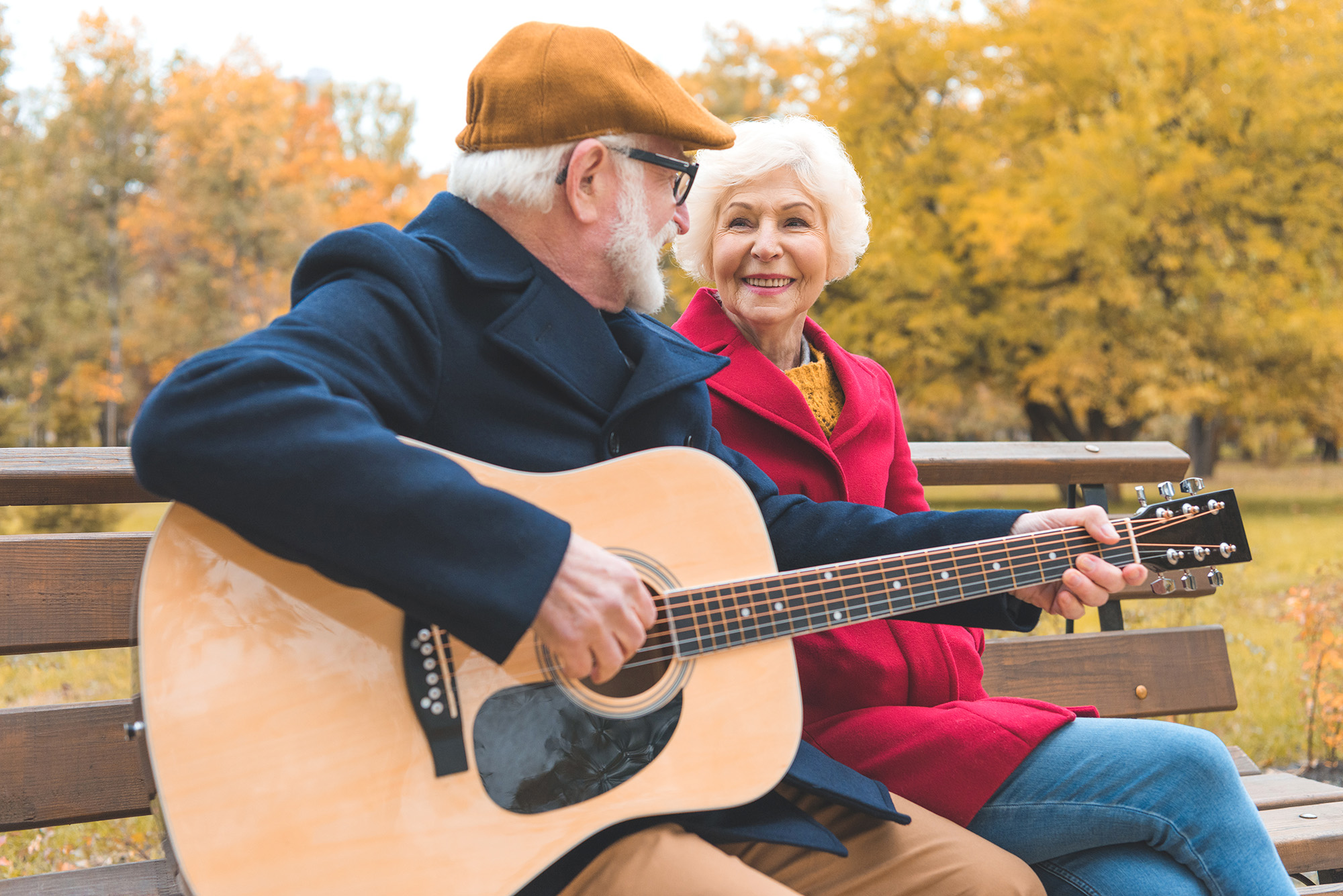 An retired couple on a park bench playing guitar