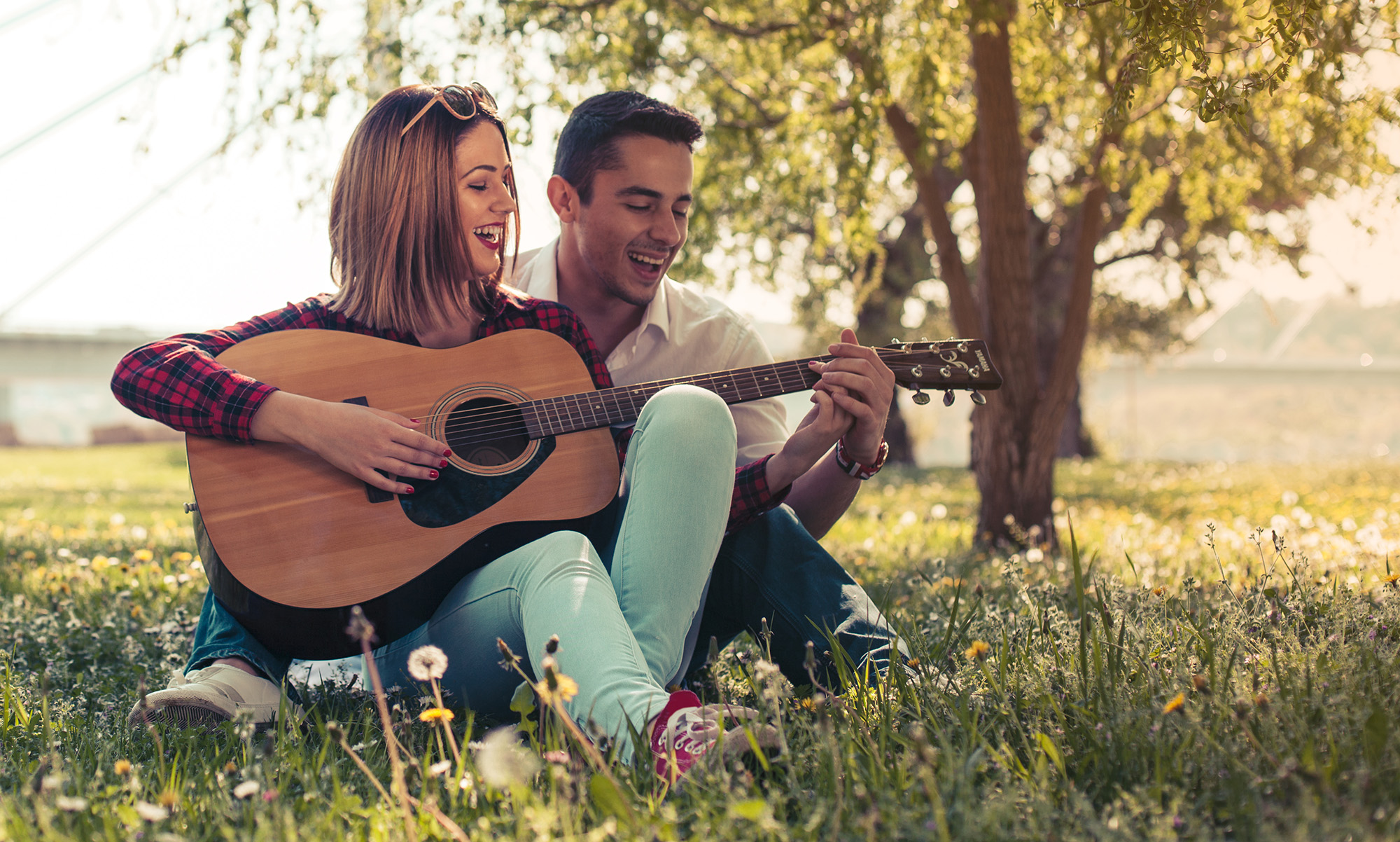 Man teaching his partner to play guitar in a field