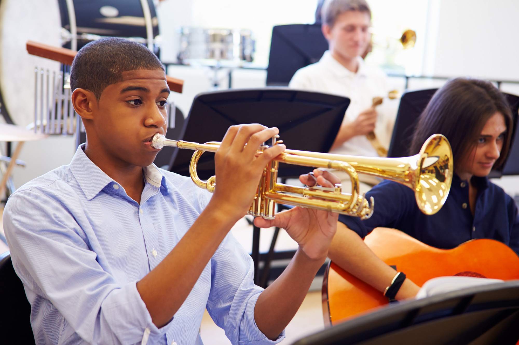 Teenage boy playing trumpet in a classroom with his schoolmates